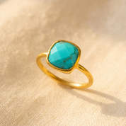 Gold turquoise cushion ring shown alone on warm textured fabric.