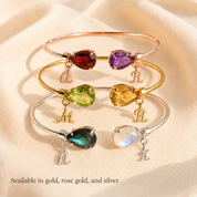 Three birthstone bangle bracelet with teardrop gemstones and initial charms, available in rose gold, gold and sterling silver for a personalized gift.