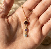 Close-up of custom birthstone necklace held in hand, showing a delicate vertical drop design with round gemstone charms.