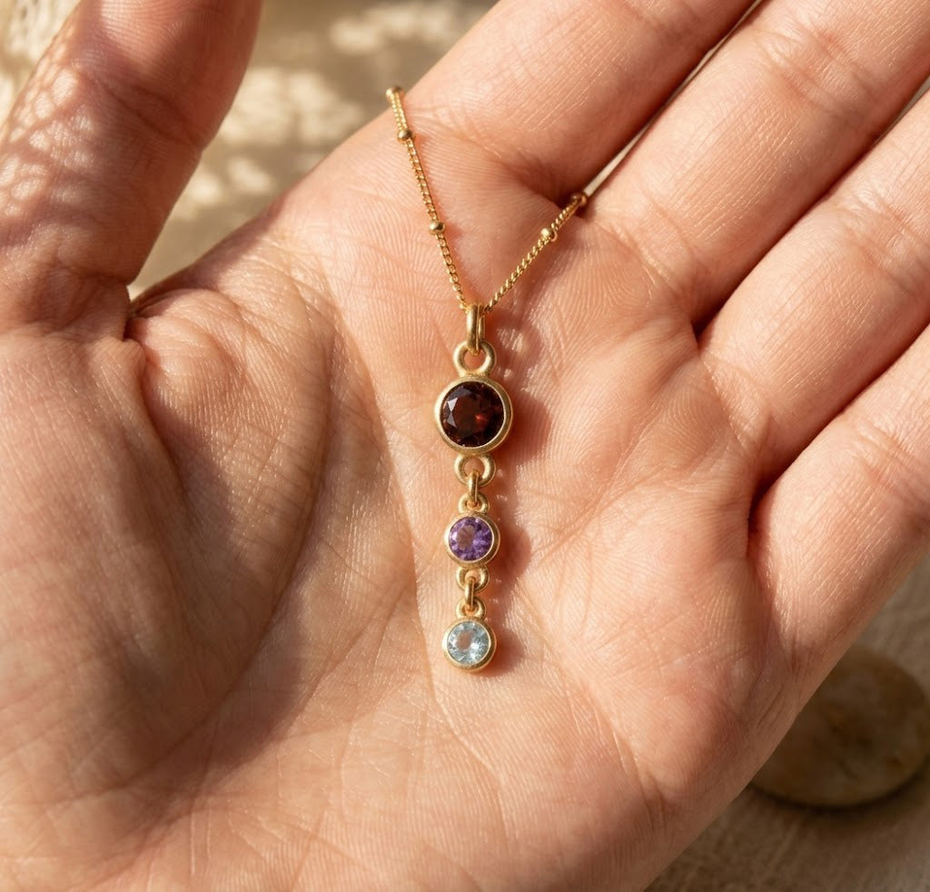 Close-up of custom birthstone necklace held in hand, showing a delicate vertical drop design with round gemstone charms.