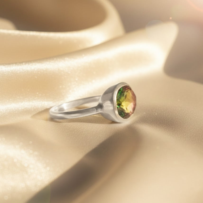 close-up of the watermelon tourmaline oval bezel ring in sterling silver on ivory backdrop, focusing on the bezel setting and faceted multicolor tourmaline slice with green-pink gradient, minimalist gemstone birthstone ring for October, perfect as a personalized gift for mom, grandma or bride, stacking friendly design, handmade artisan ring with gemstone symbolism and sleek finish.