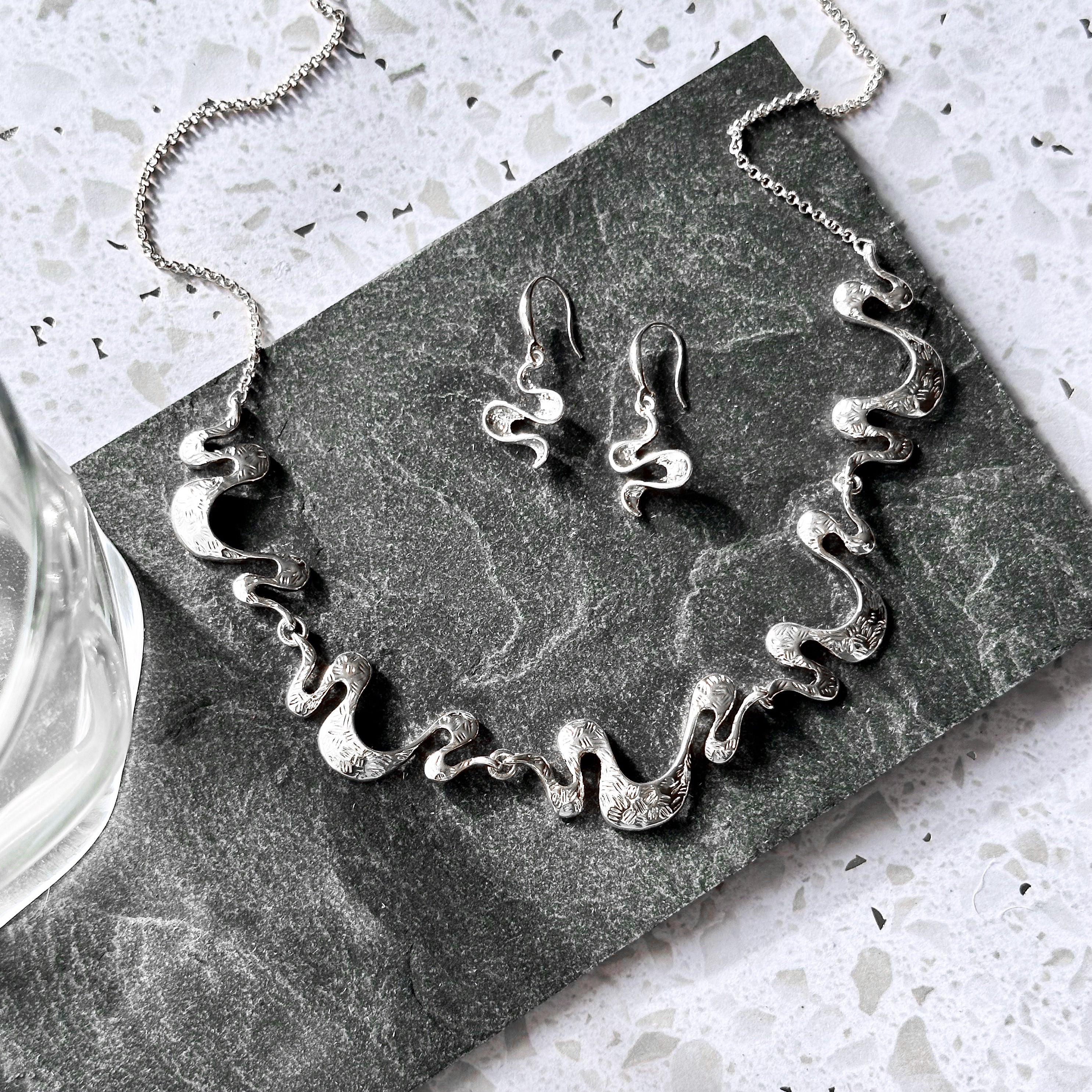 Silver wave necklace and earrings set displayed on dark stone for artistic boho jewelry styling