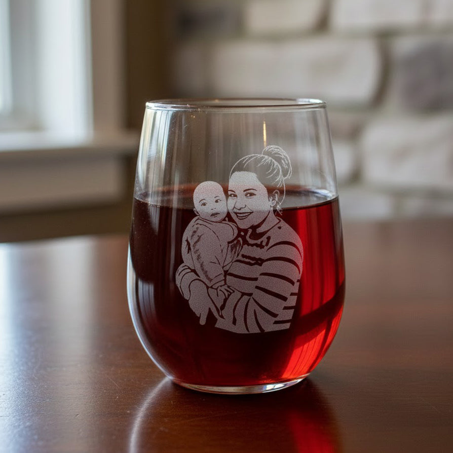 Custom photo wine glass featuring engraved portrait of mom holding baby, stemless red wine glass on table, personalized etched family illustration, unique Mother’s Day gift, custom mom wine glass with picture, sentimental new mom gift idea, keepsake home bar décor.