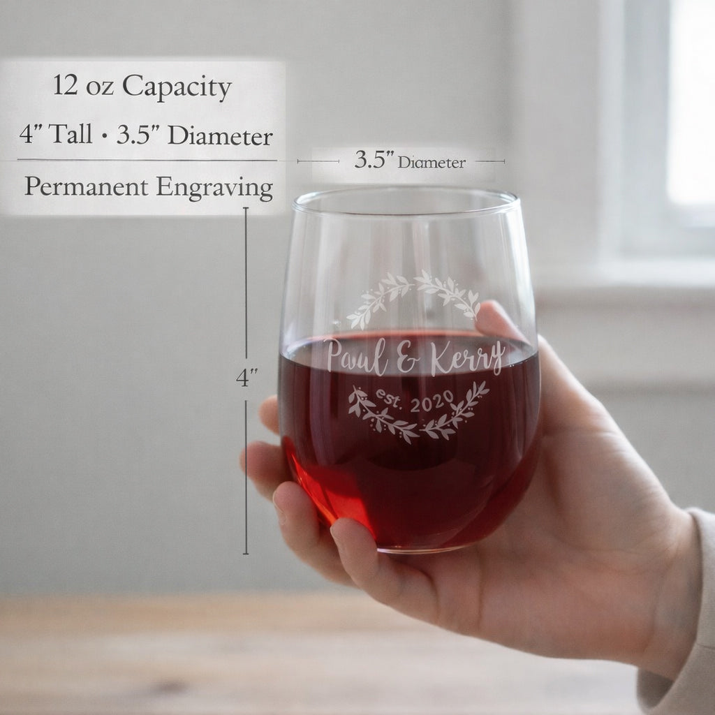 Custom engraved stemless wine glass held in hand, featuring permanent laser engraving with names and date inside a decorative wreath design. This 12 oz personalized wine glass shows size and dimensions, highlighting quality craftsmanship and durability. Ideal as a wedding gift, anniversary gift, housewarming present, or personalized glassware for couples, this engraved glass is designed for everyday use and special occasions, offering a meaningful custom keepsake that will not fade or wash off.