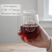 Custom engraved stemless wine glass held in hand, featuring permanent laser engraving with names and date inside a decorative wreath design. This 12 oz personalized wine glass shows size and dimensions, highlighting quality craftsmanship and durability. Ideal as a wedding gift, anniversary gift, housewarming present, or personalized glassware for couples, this engraved glass is designed for everyday use and special occasions, offering a meaningful custom keepsake that will not fade or wash off.