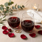 Set of two custom engraved stemless wine glasses filled with red wine, personalized with initials and romantic word engraving, styled with rose petals, wedding rings, greenery, and candlelight. These permanent laser engraved wine glasses make a meaningful gift for couples, weddings, anniversaries, engagements, or Valentine’s Day. Elegant personalized glassware designed for everyday use and special occasions, dishwasher safe and crafted as a timeless keepsake gift for him and her.