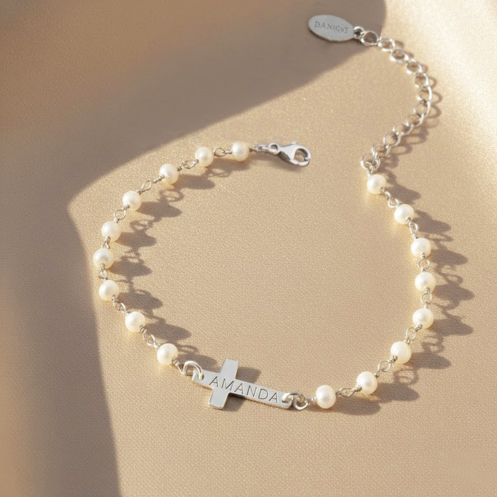Pearl bracelet with a cross charm and engraved name on a beige background. This bracelet is perfect as a baptisms, christenings or first communion gift. It also makes a lovely Christian wedding gift.