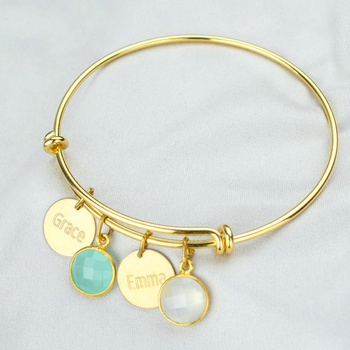 Single gold bangle bracelet with two name disks and an aqua chalcedony and moonstone birthstones with names engraved in modern thin font