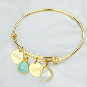 Single gold bangle bracelet with two name disks and an aqua chalcedony and moonstone birthstones with names engraved in modern thin font