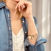 Model in white top and jean jacket is wearing out mother's bangle bracelet with engraved disk and peridot and kyanite birthstones. 