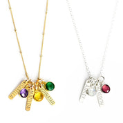 A gold filled satellite chain with tiny engraved name bars and purple amethyst, citrine and green onyx birthstones. A sterling silver cable chain with tiny engraved name tags and moonstone and garnet birthstones. Gemstones on a white background. 