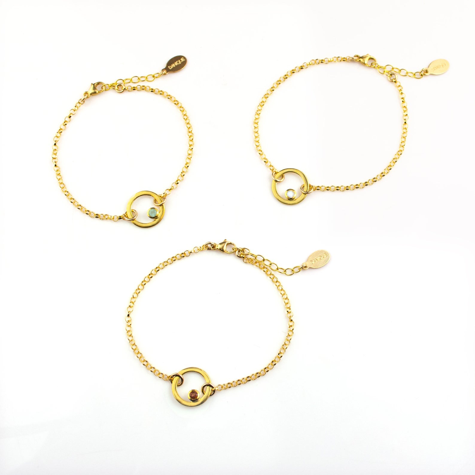 three gold plated open circle pendant charm birthstone bracelets featuring aqua chalcedony, clear quartz and garnet birthstones. March birthstone, January birthstone, april birthstones. gemstone jewelry on white background. 