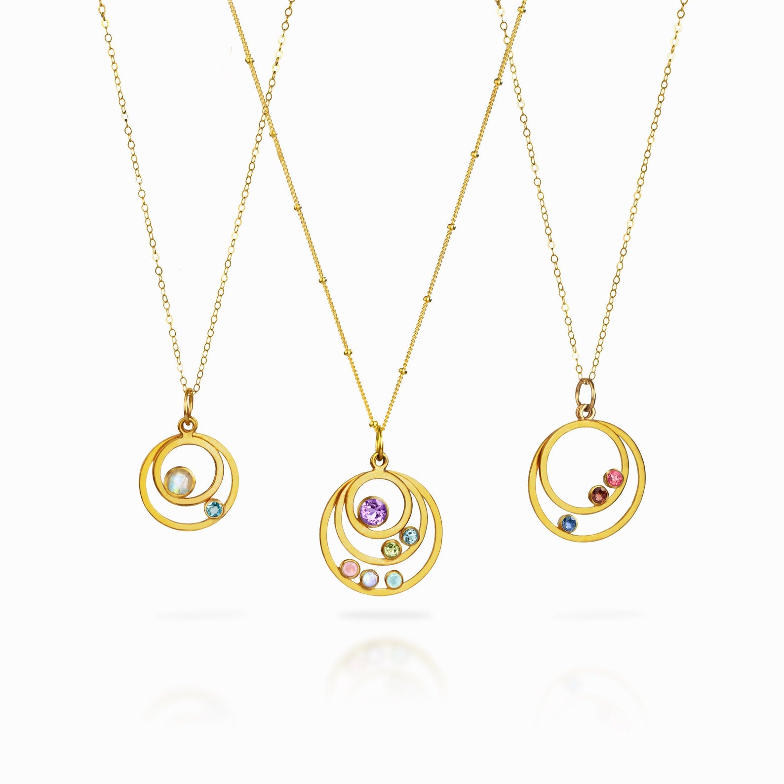 Three gold filled orbital necklace, first featuring two orbit pendants with moonstone and blue topaz. Middle necklace features a satellite chain with purple amethyst, peridot, blue topaz, pink chalcedony, moonstone and aqua chalcedony. Last necklace has garnet, ruby and kyanite birthstones