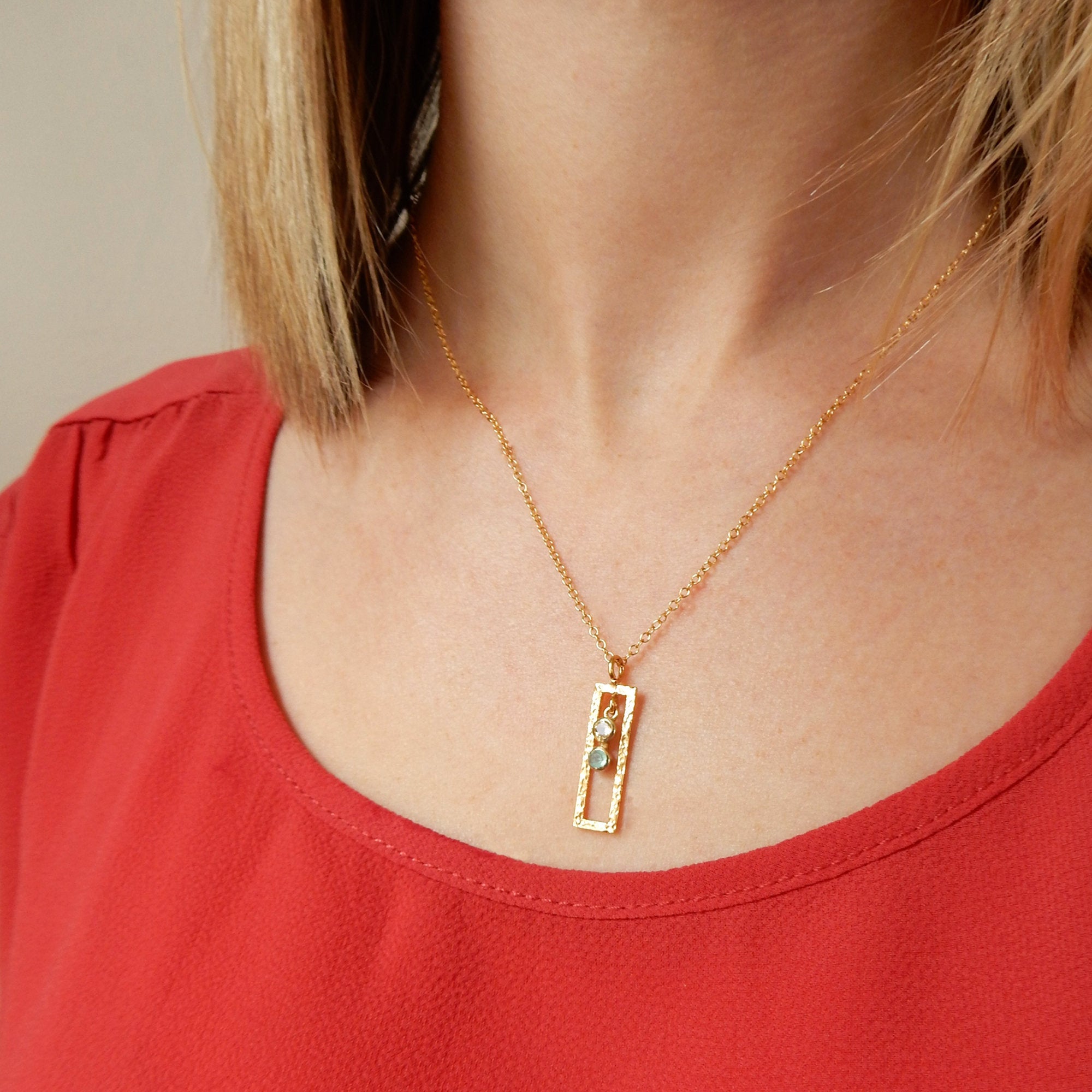 Model in a red top is wearing our gold filled open frame necklace with clear and aqua chalcedony birthstones. 