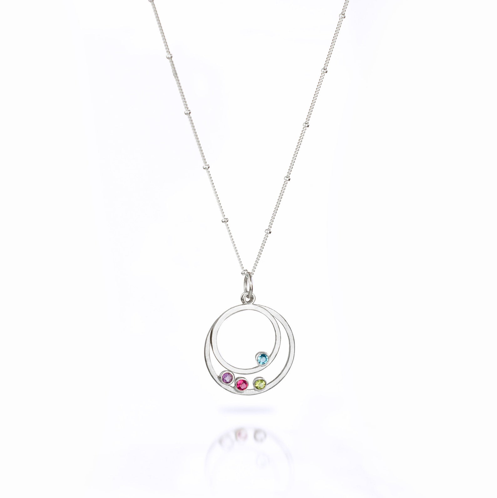 Single sterling silver satellite chain with two orbit pendants with blue topaz and purple amethyst, ruby and peridot birthstones on white background.