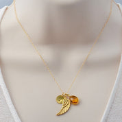Woman wearing angel wing birthstone necklace with engraved initial charm, handcrafted in vermeil gold and sterling silver, designed as a personalized remembrance jewelry gift.