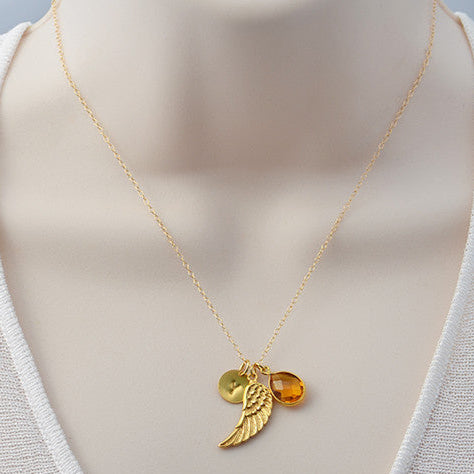Woman wearing angel wing birthstone necklace with engraved initial charm, handcrafted in vermeil gold and sterling silver, designed as a personalized remembrance jewelry gift.