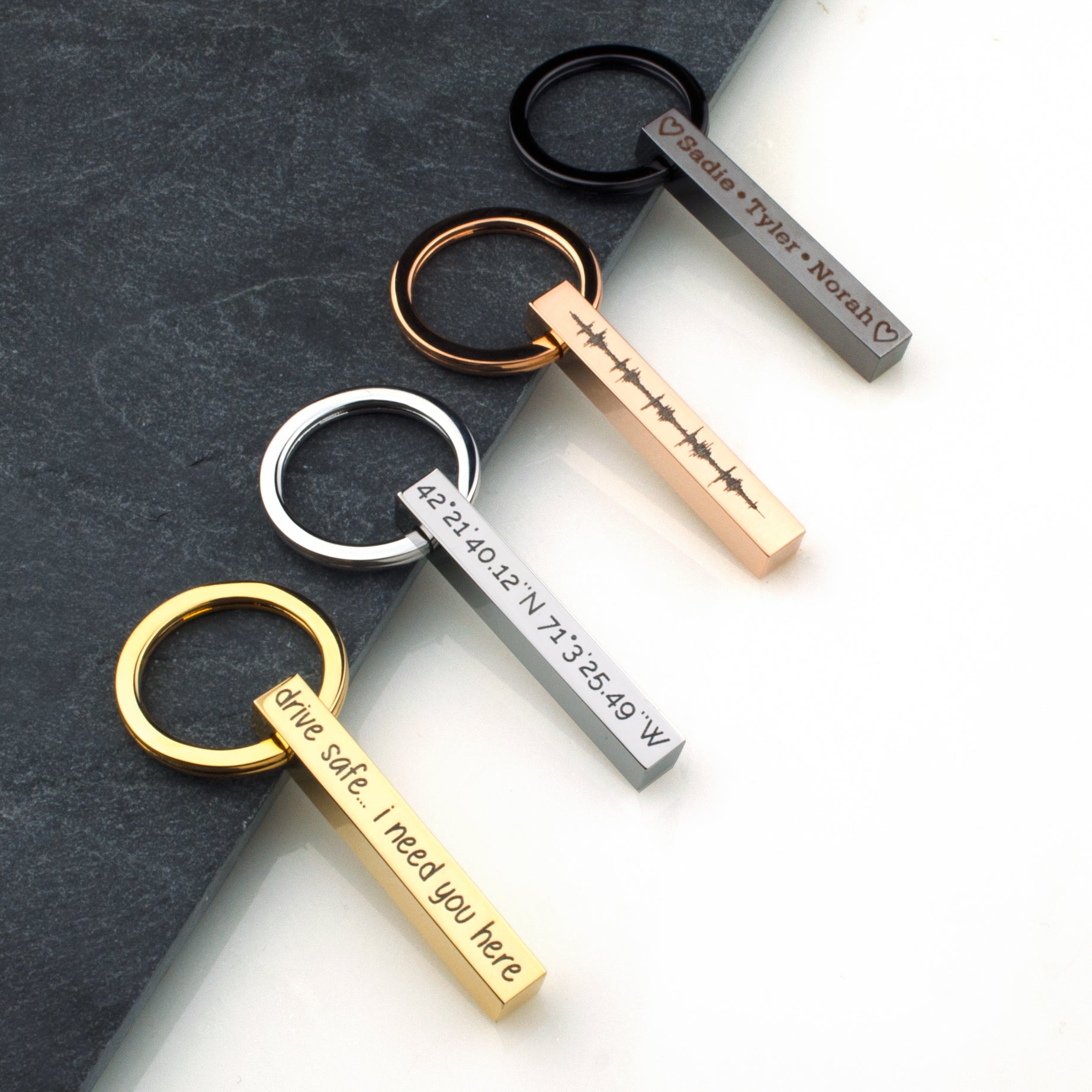 Collection of vertical bar keychains in black, silver, gold, and rose gold on a matte card, each etched with different phrases. Demonstrates color variety, deep engraving, and clean lines—ideal for monogram keyring, “drive safe I need you here” message, or matching groomsmen keychain set for weddings and bachelor party favors.
