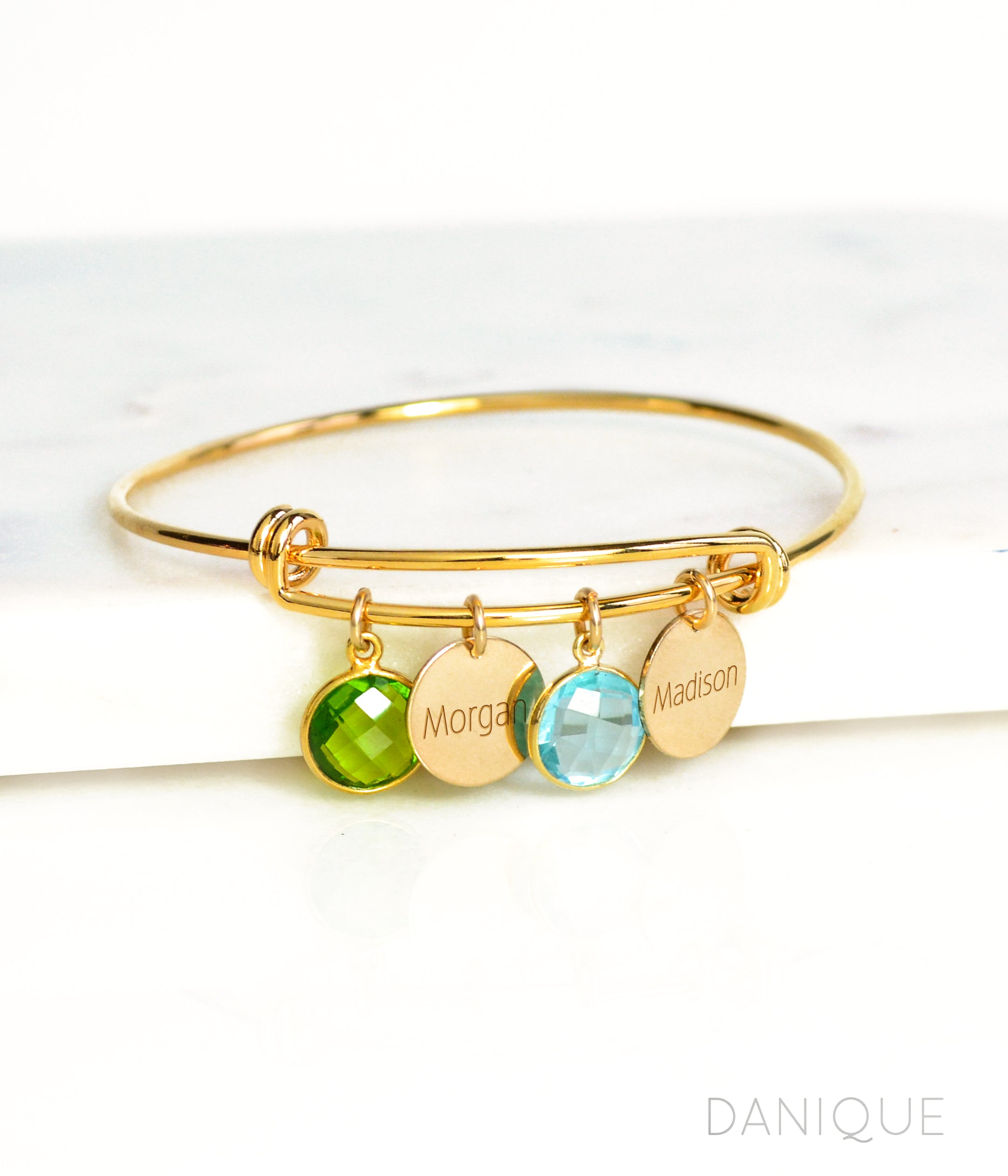 Single gold bangle bracelet with two name disks and peridot and blue quartz birthstones with names engraved in modern thin font