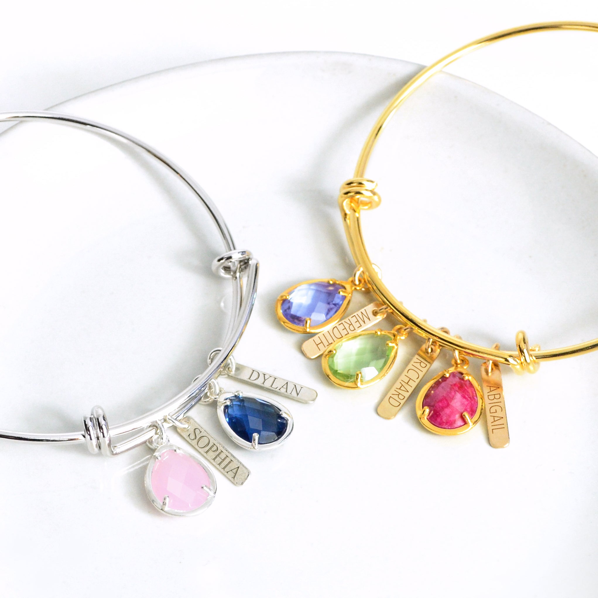 Silver birthstone and engraved name bar bangle bracelet with pink chalcedony and kyanite birthstones.
Gold birthstone and engraved name bar bangle bracelet with purple amethyst, peridot, and ruby birthstones.