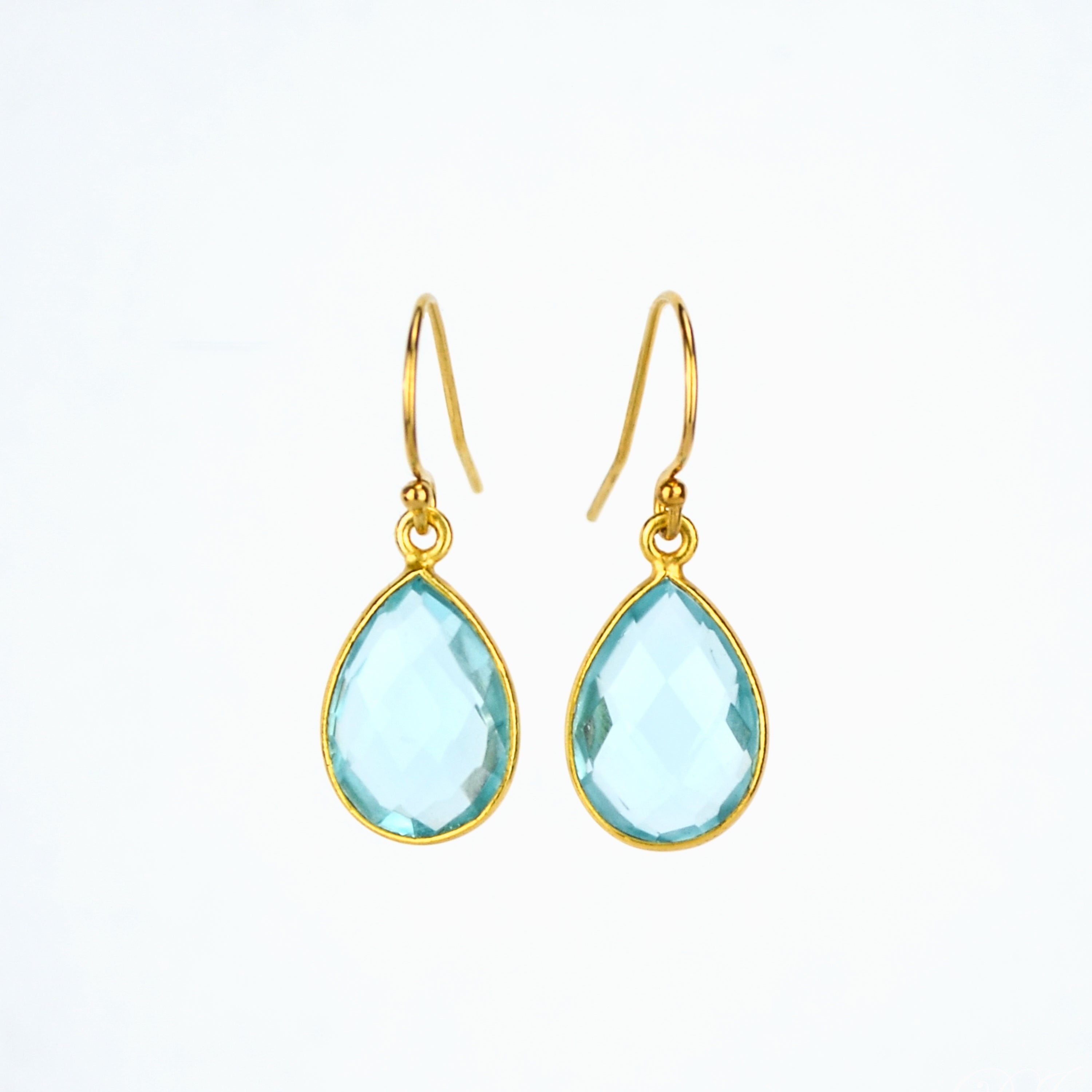 Gold blue topaz teardrop dangle earrings on a white background. Blue topaz birthstone, december birthstone, blue topaz gemstone, december gemstone. 