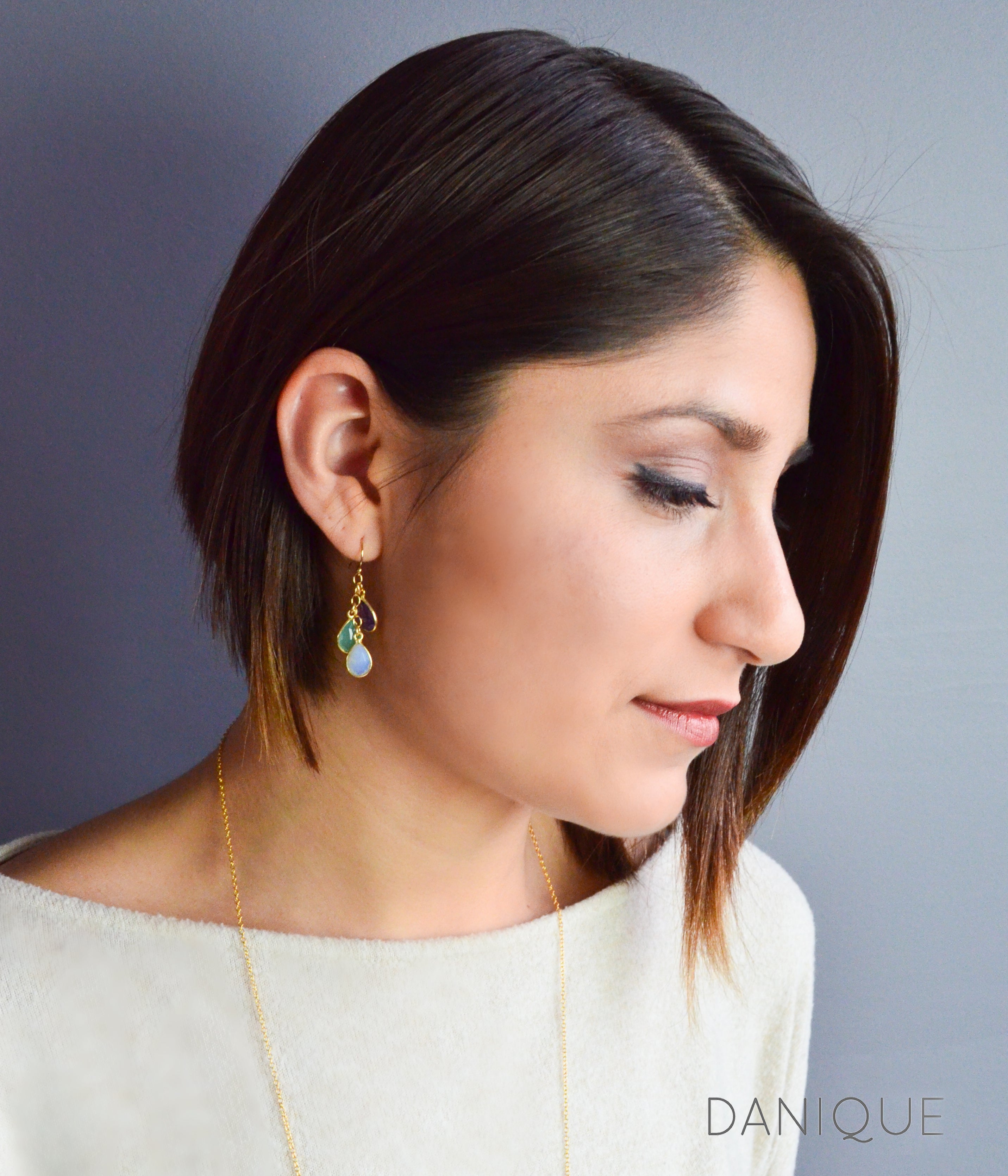 Model is wearing gold cascade earrings with purple amethyst, green onyx and moonstone.