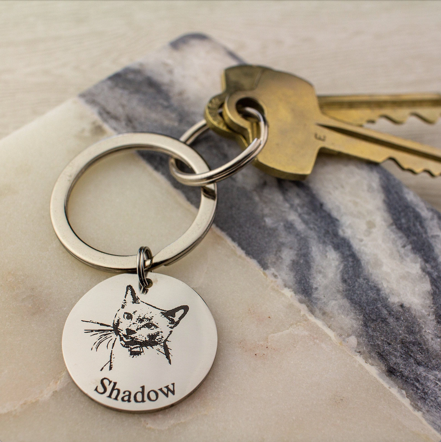 keys attached to a silver toned circle keychain with cat image and name engraved in classic font.