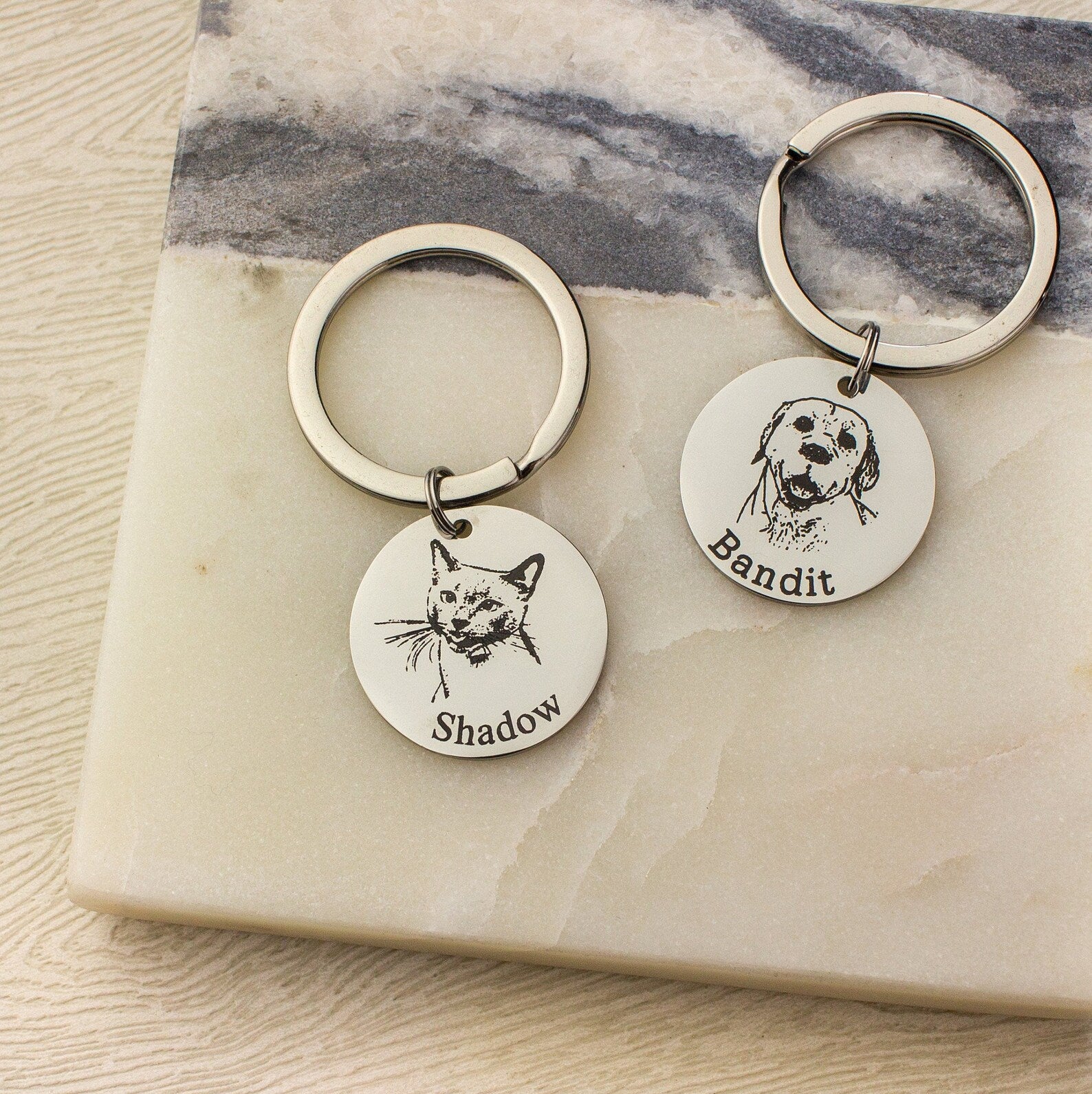 Two silver toned circle keychains with cat image and name engraved in classic font and dog with typewriter font.