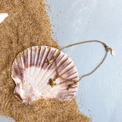 Single gold filled charm anklet with seashell, turtle and dolphin charms and lobster clasp sitting in a seashell and sand. 