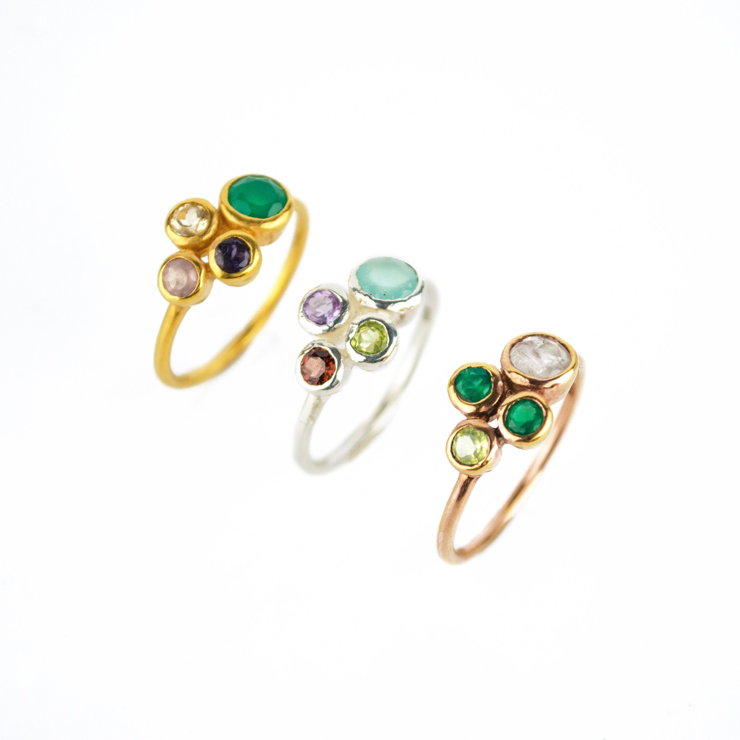 Single gold plated custom mother of three birthstone ring. Mom stone is green onyx, kid's stones are pink chalcedony, kyanite and citrine. Center is a sterling silver ring with aqua chalcedony, purple amethyst, garnet and peridot. Single rose gold plated ring with moonstone, two green onyx and peridot birthstones. 