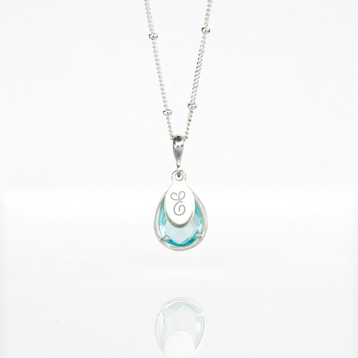 Sterling silver satellite December Sky Blue Quartz Necklace with personalized engraved script initial tag on white background. Teardrop birthstone december gemstone december birthday light blue
