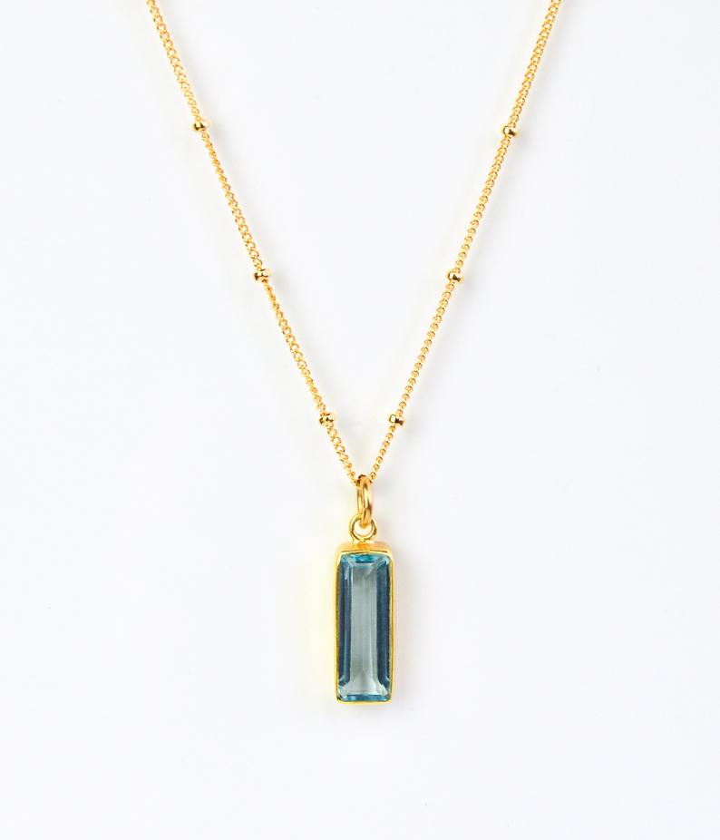 Single gold filled satellite chain with vertical sky blue gemstone december birthstone adira bar necklace on white background
