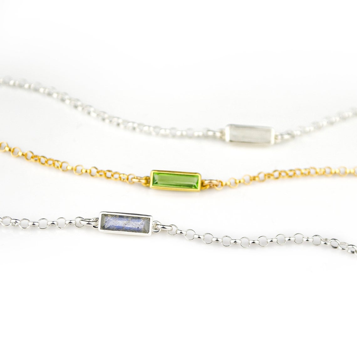 Three alternating silver and gold chain adira bar bracelets featuring, moonstone, peridot and labradorite birthstones on white background
