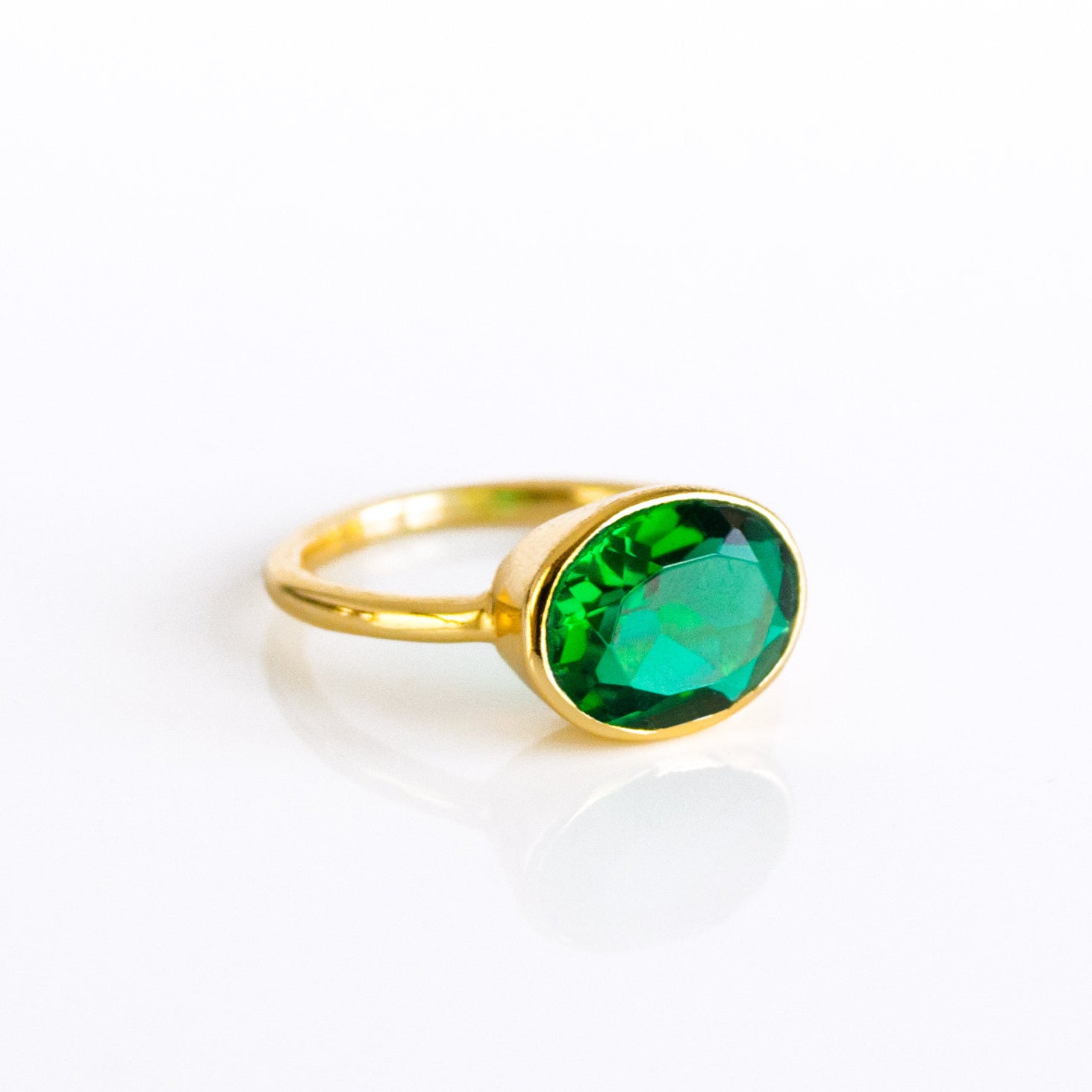 A modern oval emerald ring with bezel setting in gold vermeil, featuring a vivid green emerald-color quartz (8×12 mm) on a slim stackable band. Handmade in the USA, this May birthstone ring is available in sizes 5–10 and offered in sterling silver and rose gold vermeil as well. A dainty yet eye-catching green gemstone ring—perfect for birthdays, anniversaries, or everyday minimalist style.