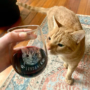 Custom cat photo wine glass with engraved pet portrait and name “Sundance,” stemless red wine glass held beside matching ginger cat on rug, personalized etched cat lover gift, custom pet wine glass for birthdays, holidays, or memorial keepsake.