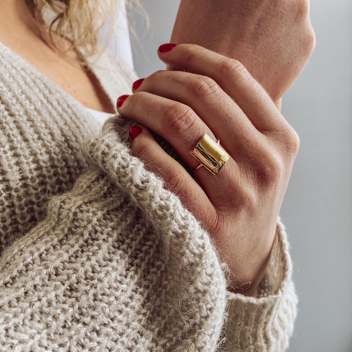 Model in white sweater is wearing a gold plated engraved rectangle nameplate ring. name plate ring, bar, statement ring. 