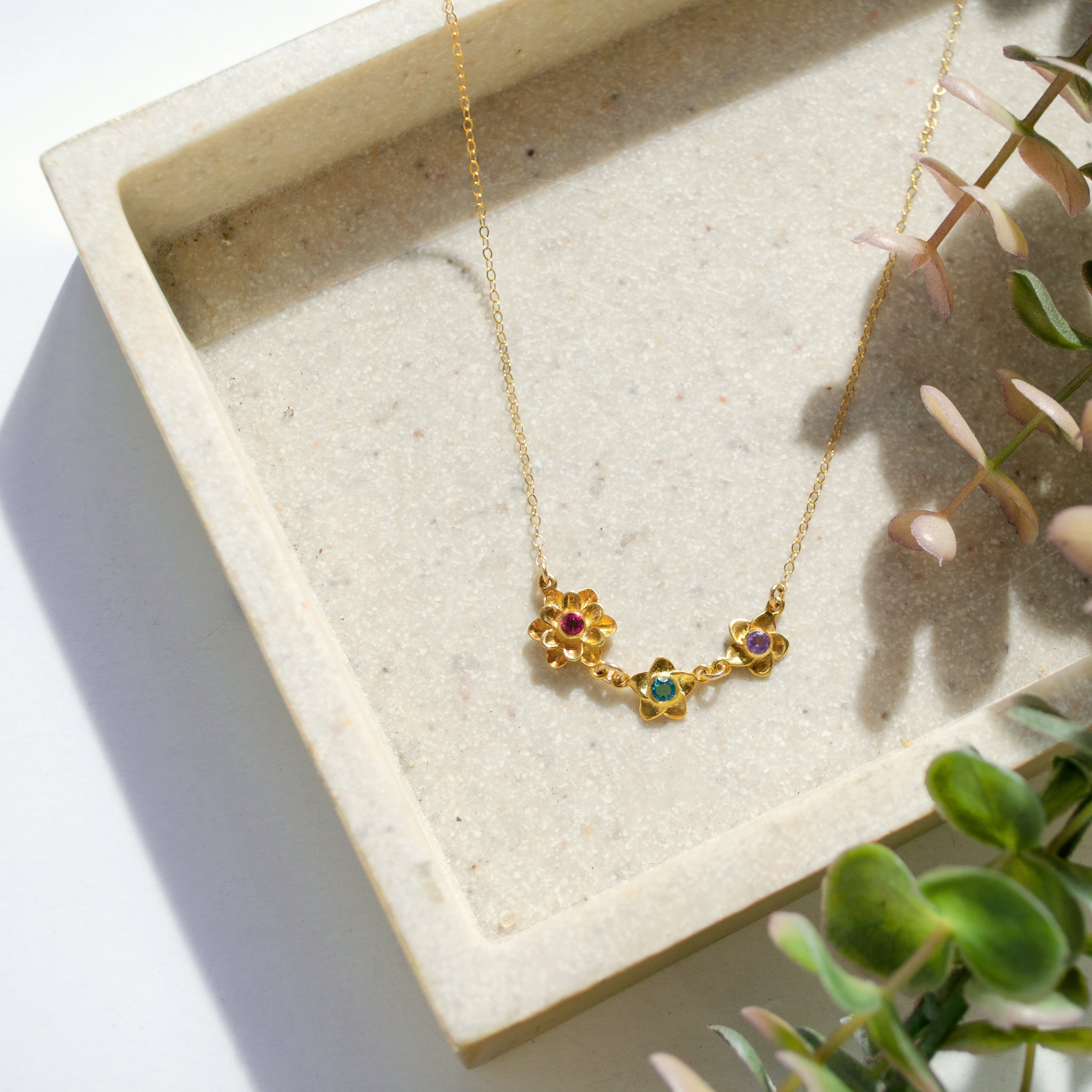 Gold filled bloom necklace with three flower pendants with garnet, green onyx and purple amethyst birthstones. Mom of two necklace.