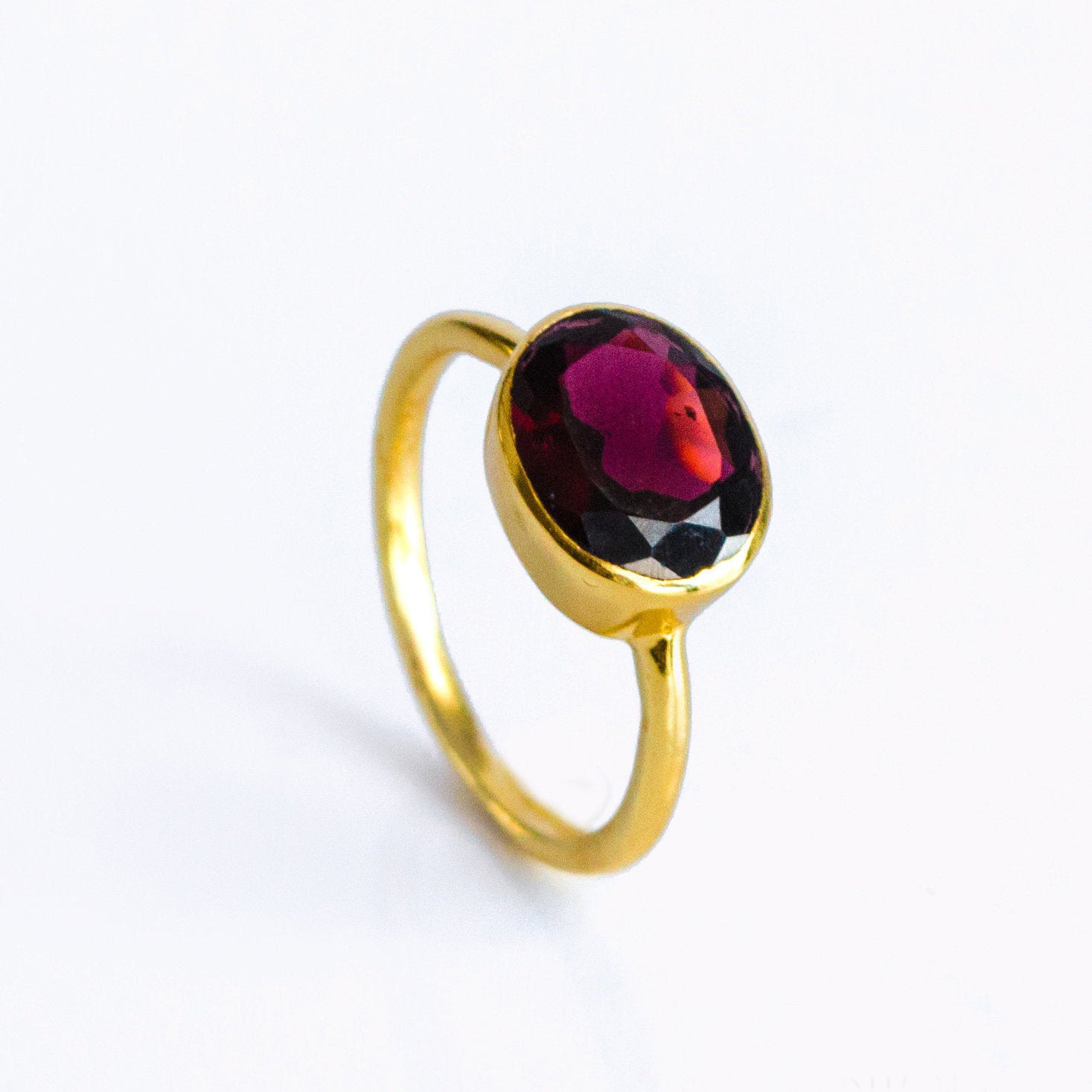 Oval garnet bezel set ring in gold vermeil, solitaire January birthstone ring with faceted red gemstone; minimalist stackable cocktail ring for women; dainty oval gemstone jewelry handcrafted in sterling silver or 18k gold vermeil; everyday ring, promise or anniversary gift for her; sizes 5–10; timeless oval bezel setting for secure, snag-free wear; Danique Jewelry birthstone collection.