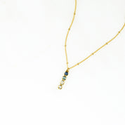 Gold filled birthstone bar necklace with bezel-set Birthstones: September Sapphire, June Moonstone, December Blue Topaz, April Clear Quartz displayed in a flat lay against a satin background. Minimalist personalized necklace design allows up to six birthstones. Ideal jewelry gift for moms, grandmothers, wives, or daughters for Christmas, Mother’s Day, birthdays, or anniversaries.