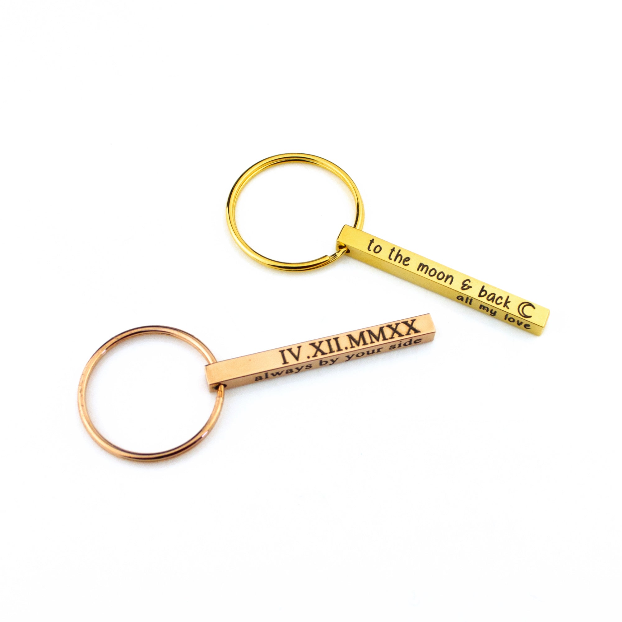 Pair of slim bar keychains in gold and rose gold finishes displayed on a clean white backdrop, each etched with short phrases to show character limits on the dainty bar. Matching spring rings keep the minimalist profile sleek. Great custom bar keychain option for couples, bridesmaids or groomsmen keychain gifts, new-driver reminders, and short motivational quotes.