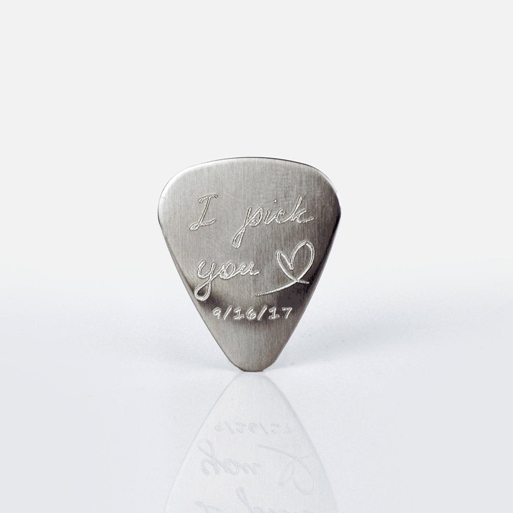 Single guitar pick with I pick you design, heart and date engraved on white background.