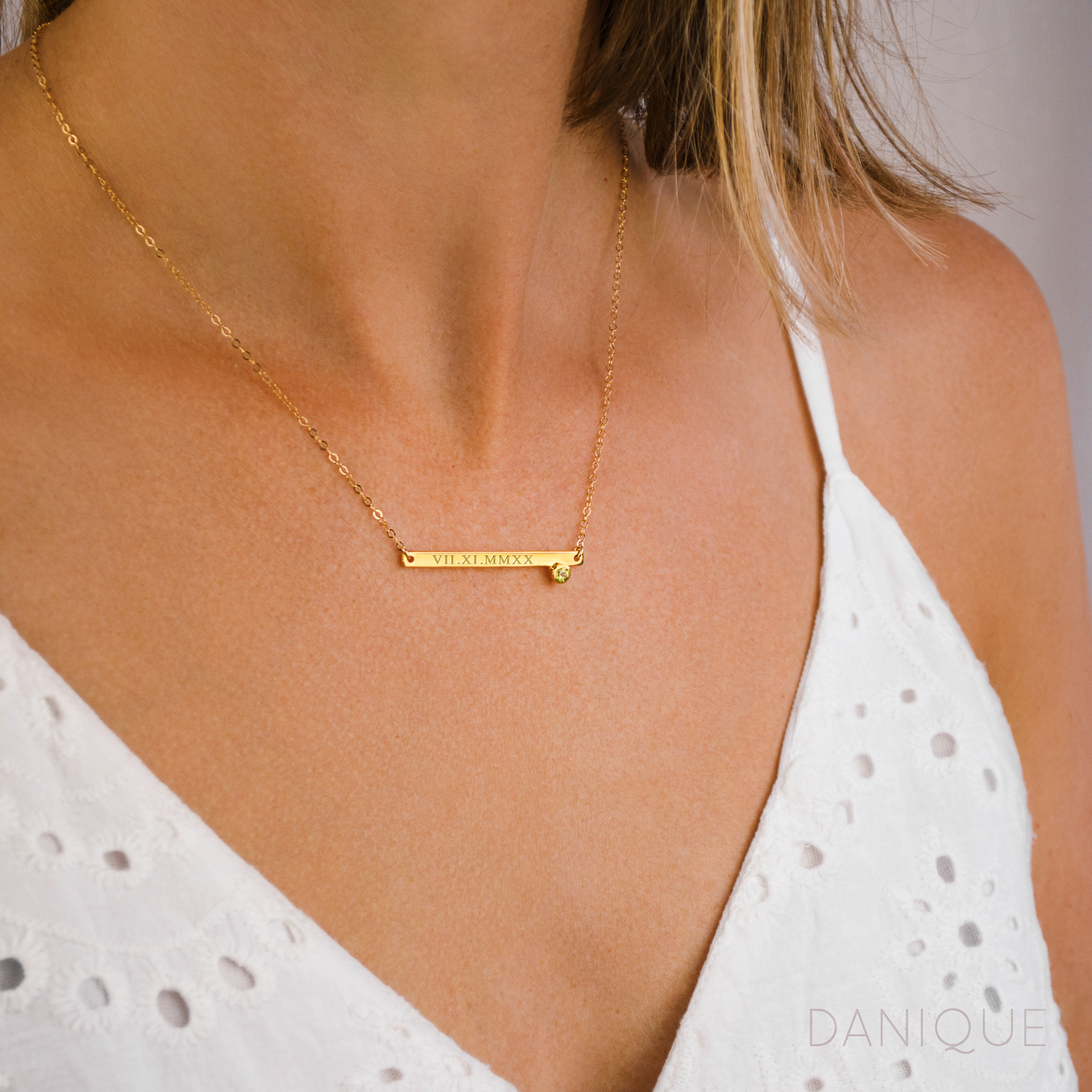 Model in white top is wearing a single Gold plated skinny bar with 1 peridot gemstone and roman numerals. 