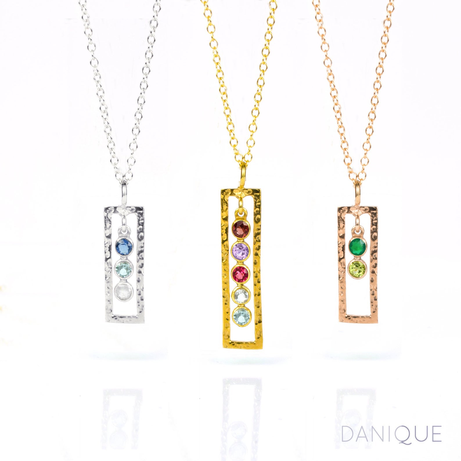 Three open frame vertical birthstone necklaces. One silver open frame necklace with kyanite, blue topaz and moonstone birthstones. Middle gold filled open frame necklace featuring 5 birthstones including garnet, purple amethyst, ruby, green amethyst and blue topaz. Last rose gold filled necklace with green onyx and peridot birthstones. 
