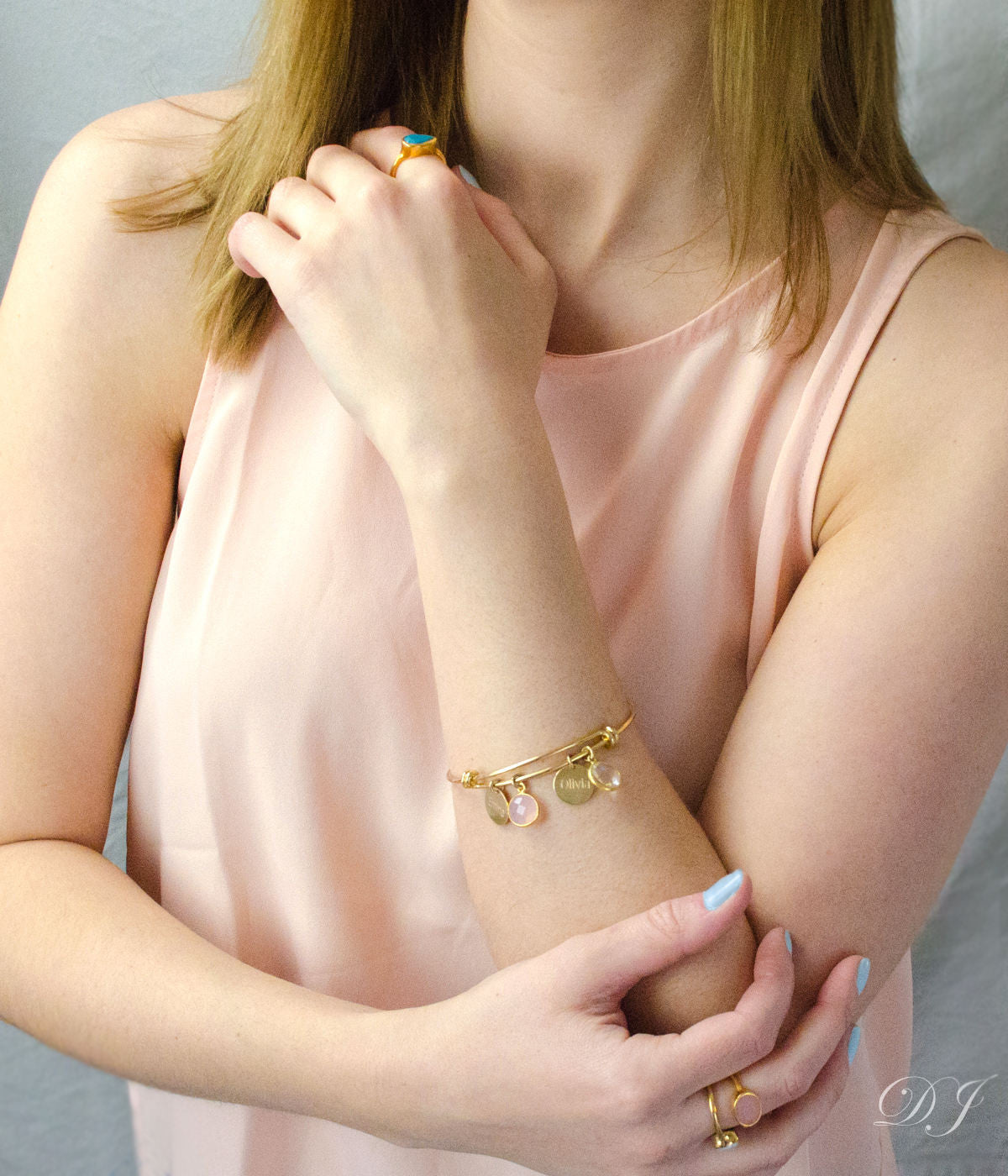 Model in beige top is wearing the name bangle bracelet with pink chalcedony and clear quartz birthstones. 
