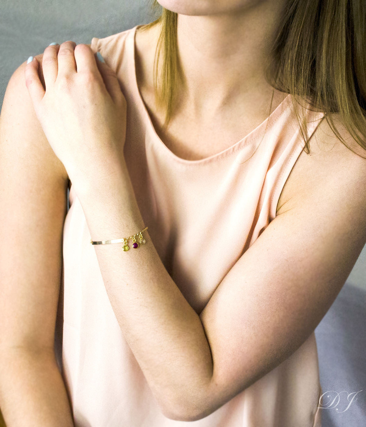 Model in cream top is wearing our dainty bar bracelet in gold with three birthstones including peridot, ruby and clear. 