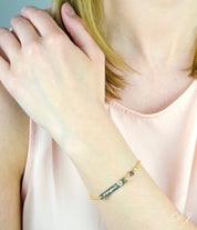 Model in pink top is wearing a gold filled footprint name engraved bar bracelet with purple amethyst gemstone. 