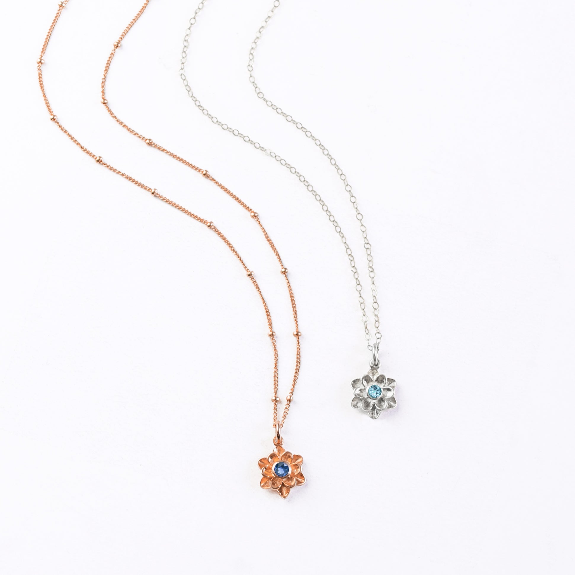 Rose gold filled satellite chain with mothers bloom flower pendant and kyanite birthstone. Sterling silver cable chain mothers bloom pendant necklace with blue quartz birthstone on white background. 