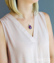 Model in cream top is wearing  a sterling silver mothers teardrop necklace with a large purple amethyst stone and two small round aqua chalcedony and kyanite birthstones.