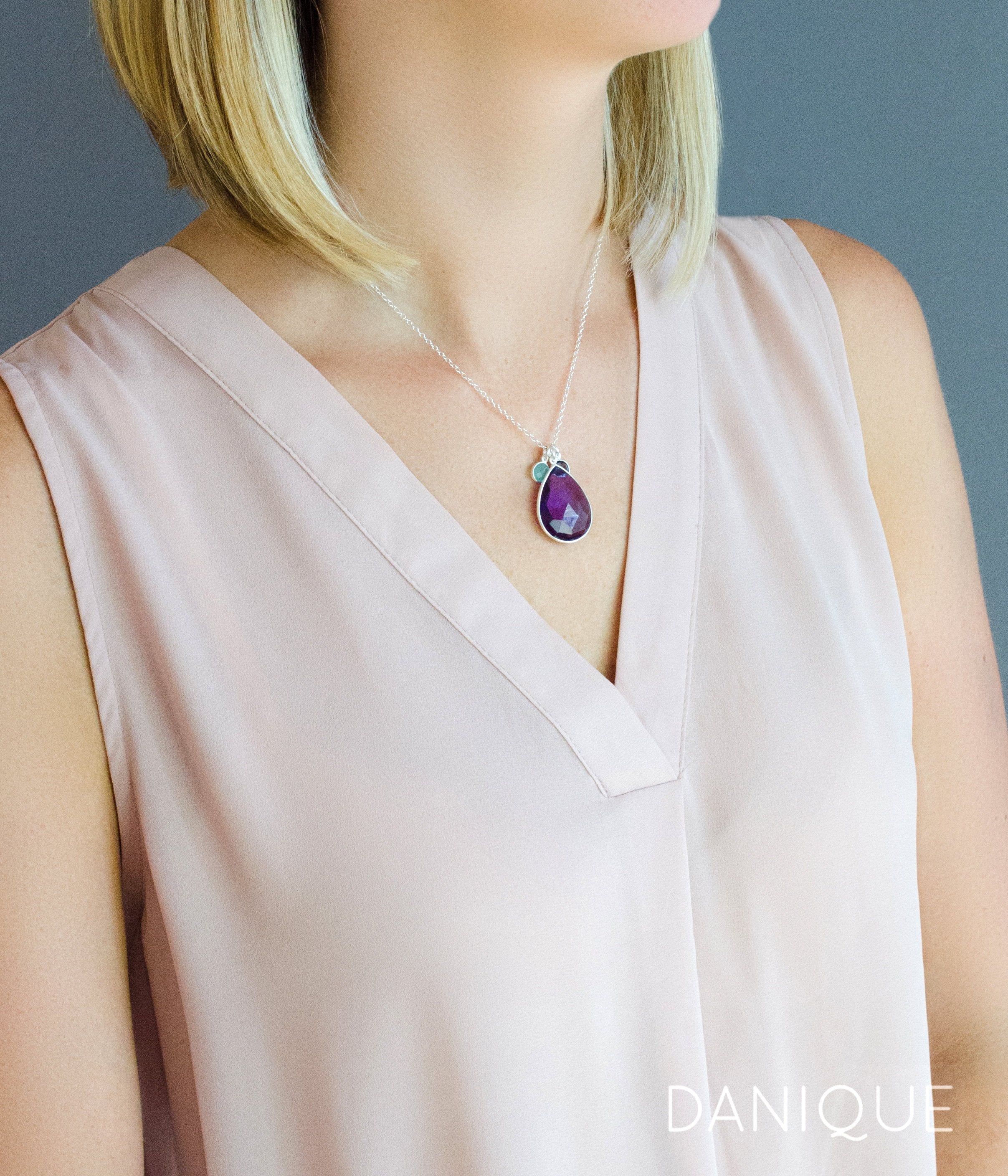 Model in cream top is wearing  a sterling silver mothers teardrop necklace with a large purple amethyst stone and two small round aqua chalcedony and kyanite birthstones.