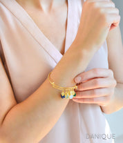 Model in cream top is wearing a single gold bangle bracelet with stamped leaf charms and lapis, aqua chalcedony, opalite and green onyx birthstones.